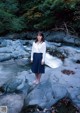 A woman standing on a rock in the middle of a stream.